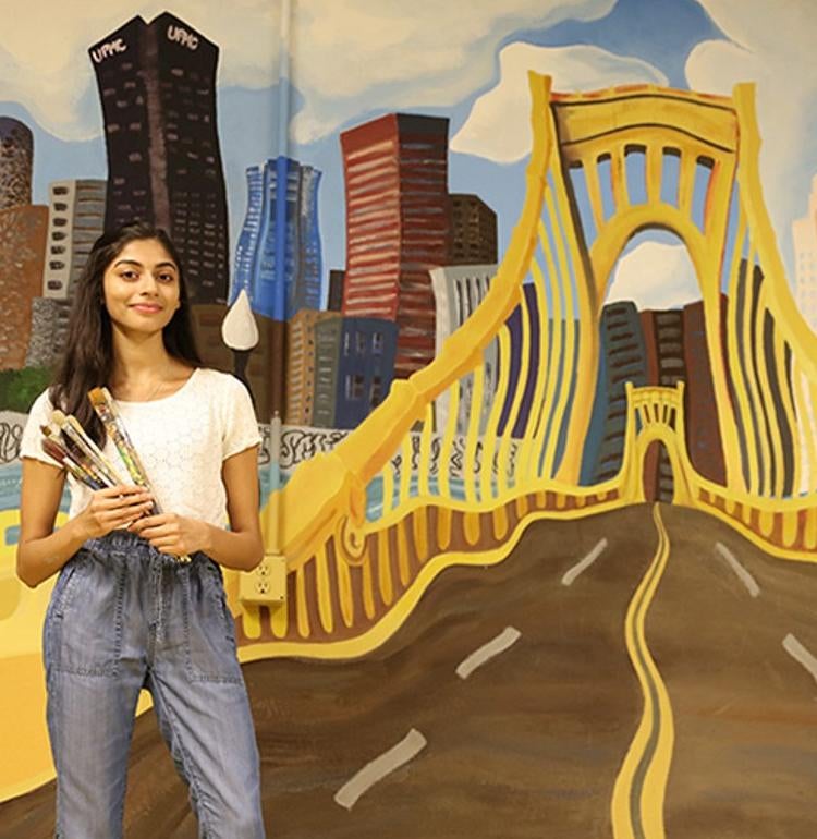 Person standing in front of a bridge painting with paint brushes in her hand